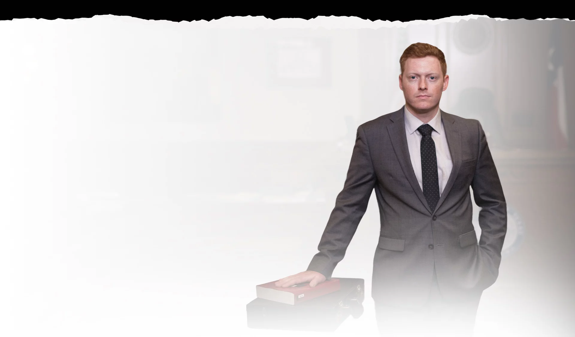 Professional male in a suit stands confidently with a hand on a legal book, symbolizing authority in a courtroom.